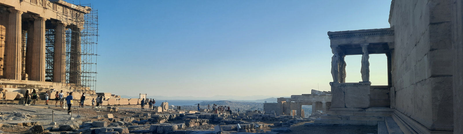 The Parthenon's colonnade (with scaffolding) and the Erechtheion's Porch of the Caryatids on the Acropolis in Athens, with the city and coastline visible in the distance, July 2022. Photo: Markus, The Philosopher's Shirt.