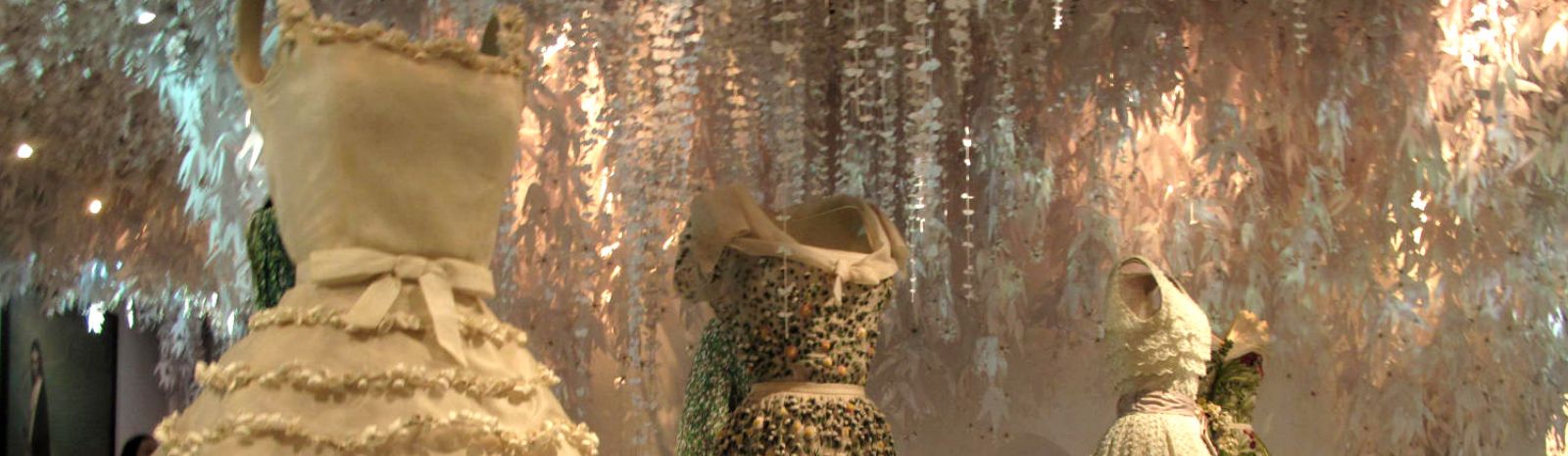 Several dresses on dressforms  in front of a glittery background.